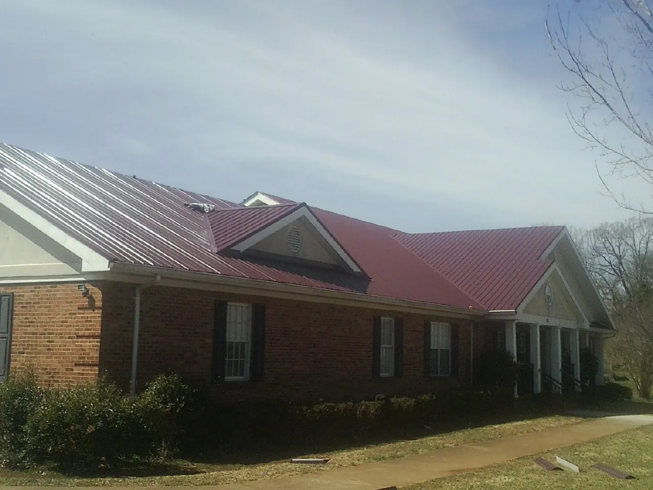 Red metal roof with gabled entries on a long brick building, from a Hail Damage Roof Repair job in Heath