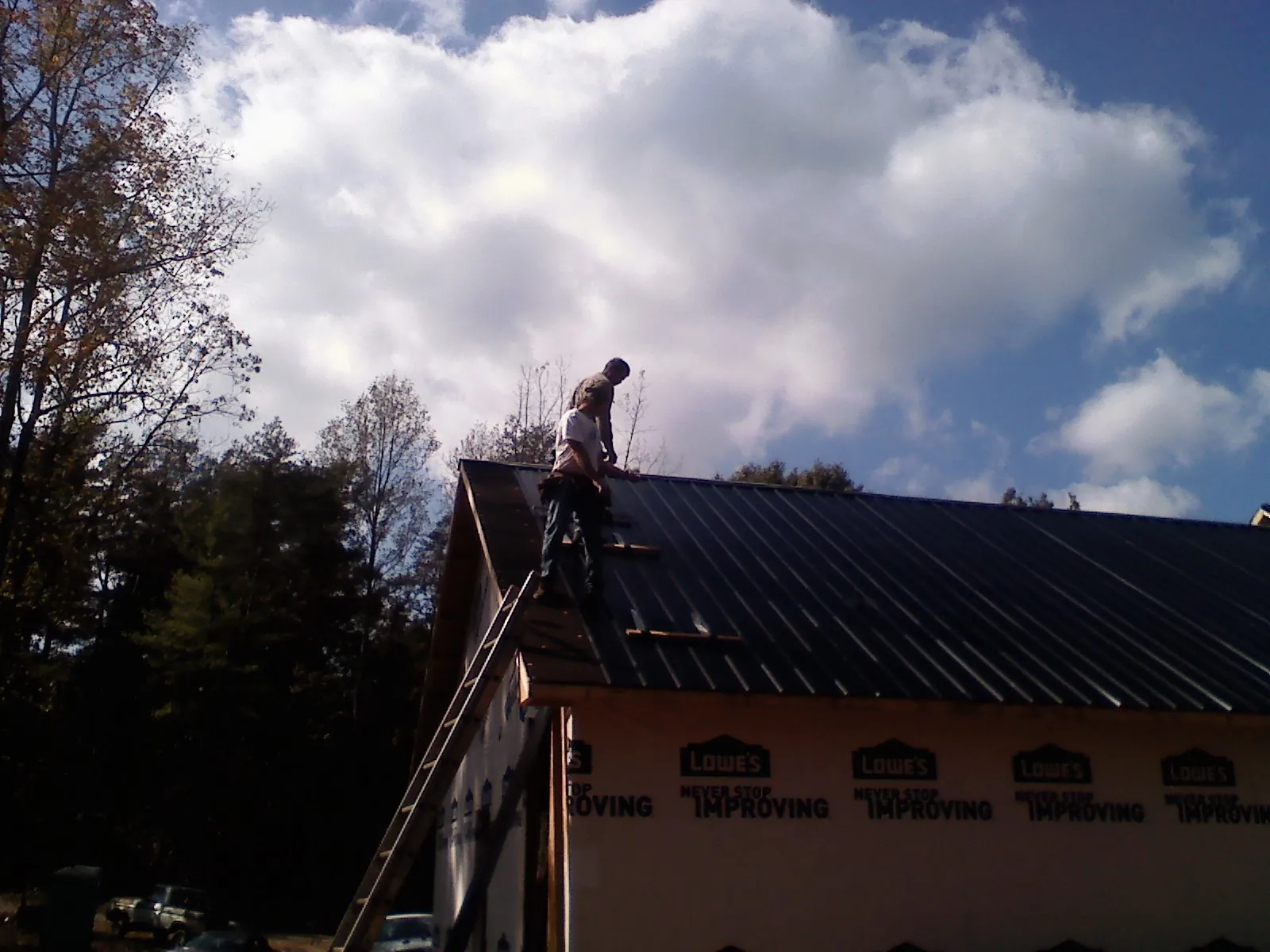 Roofer fastening dark metal panels high against a cloudy sky, from a Roof Inspection job in Heath