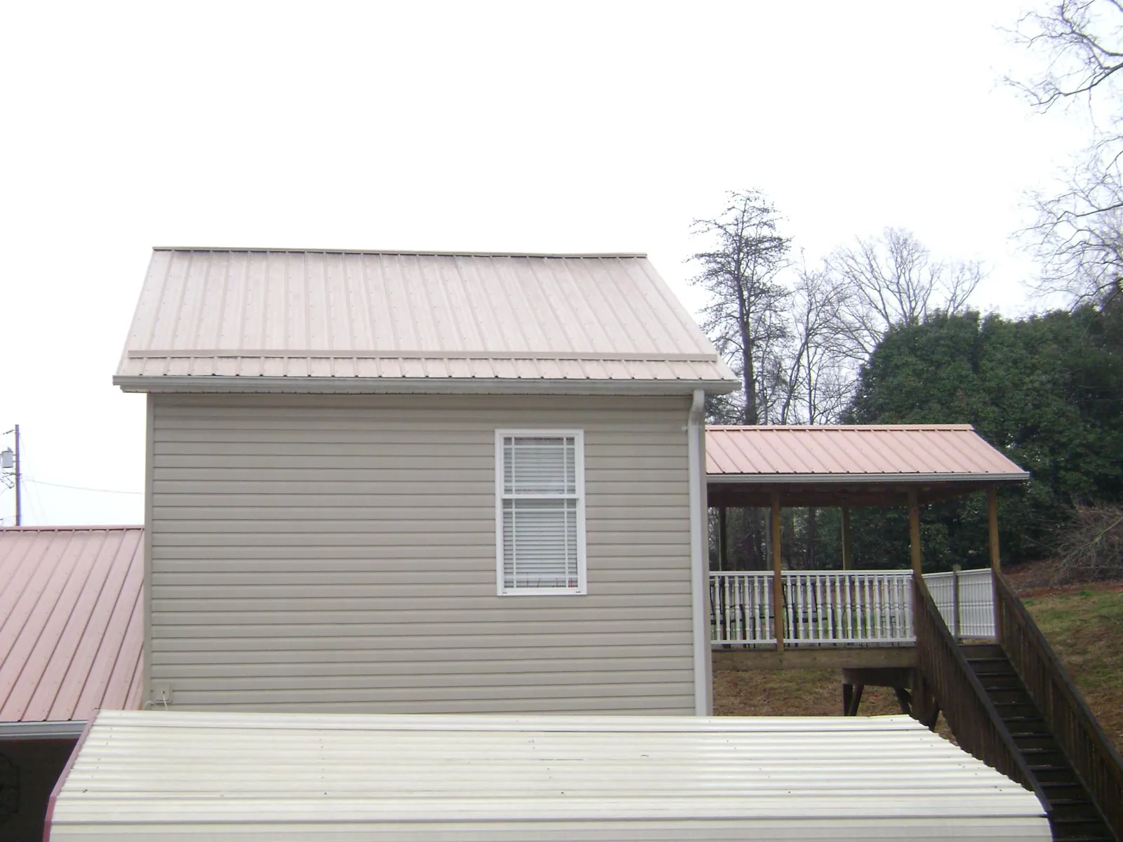 Tan metal roofs on a two story addition and attached porch, from a Roof Replacement job in Heath